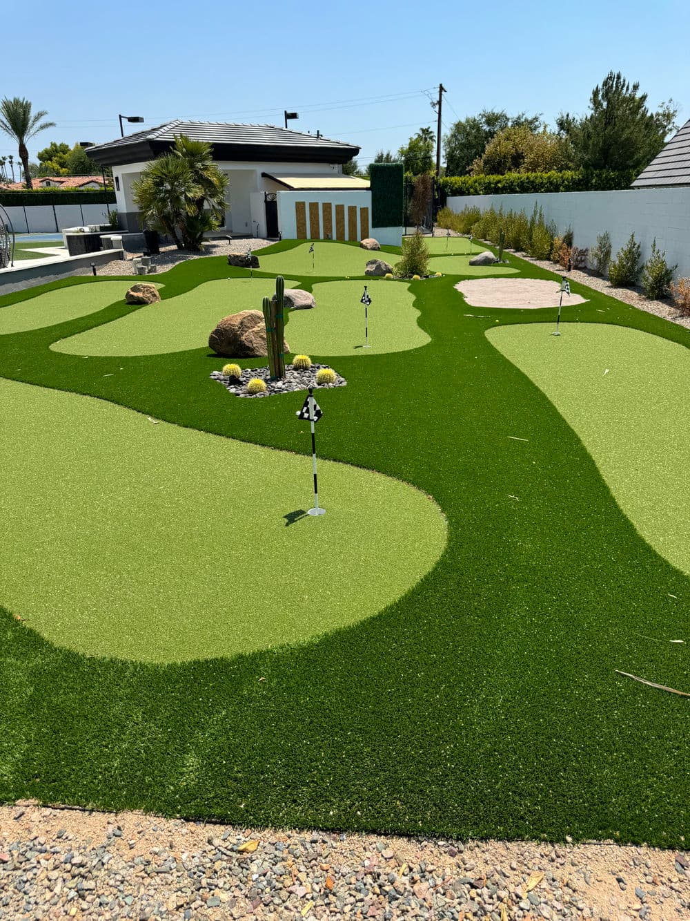 Artificial turf golf putting green with rocks and landscaping in a residential backyard.