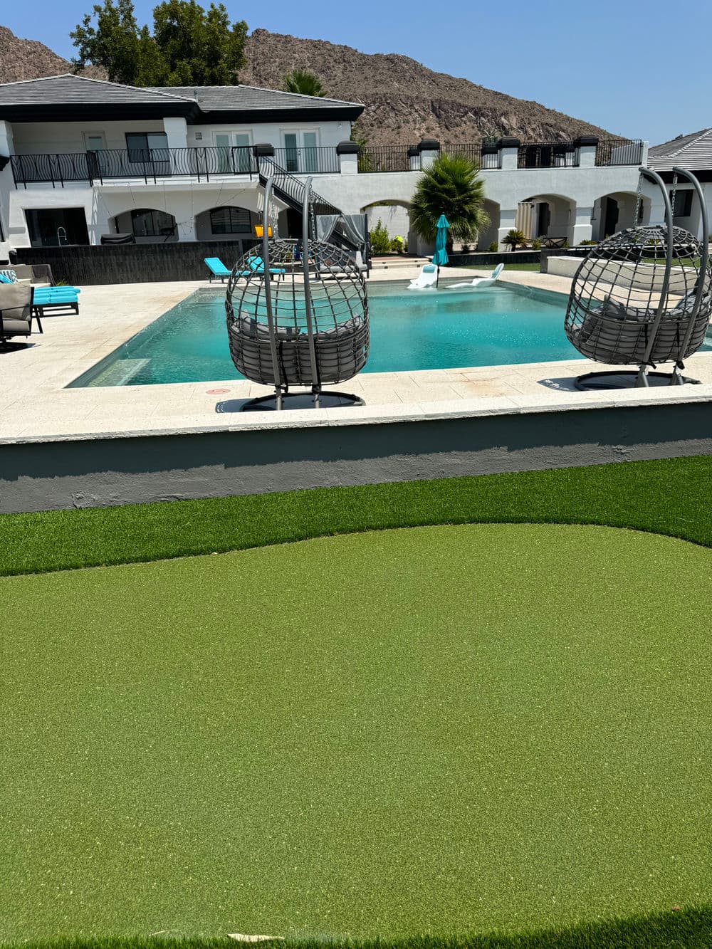 Luxury backyard with a swimming pool, hanging chairs, and green turf area. Mountain views.