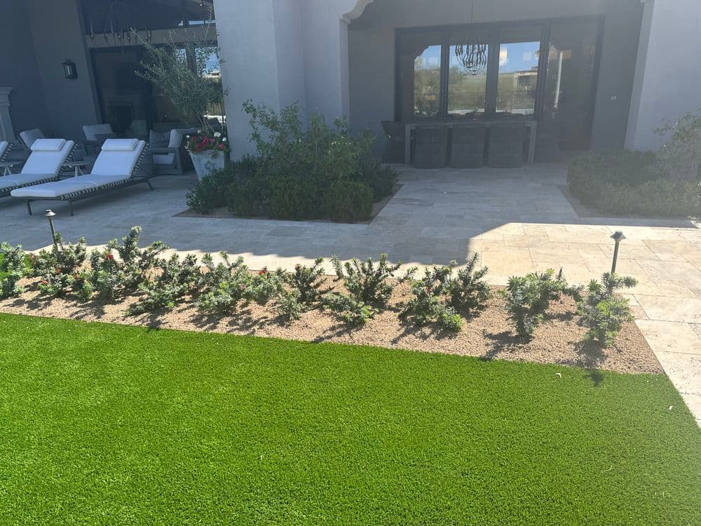 Lush green lawn and landscaped garden with stone patio and outdoor seating area.