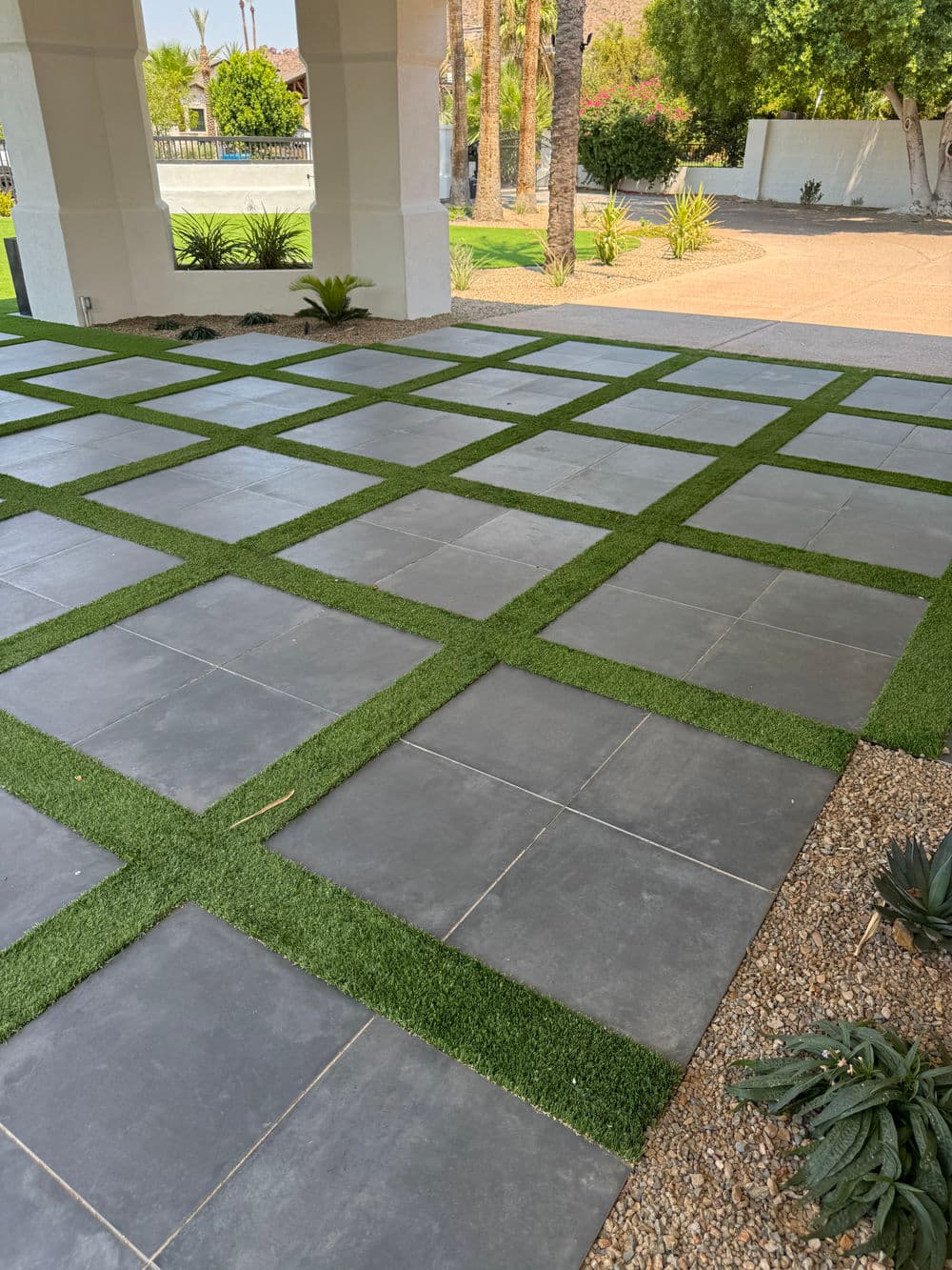 Modern patio design featuring gray stone pavers and lush green turf in a landscaped setting.