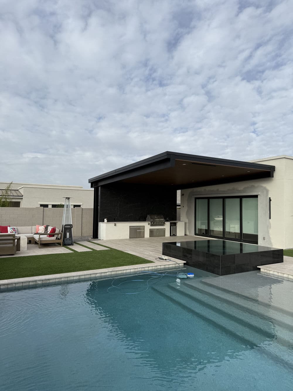 Modern backyard oasis featuring a pool, outdoor grill, and lounge seating under a cloudy sky.