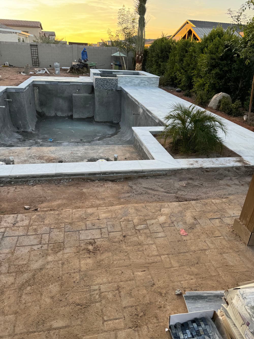 Partially constructed residential swimming pool with surrounding concrete deck at sunset.