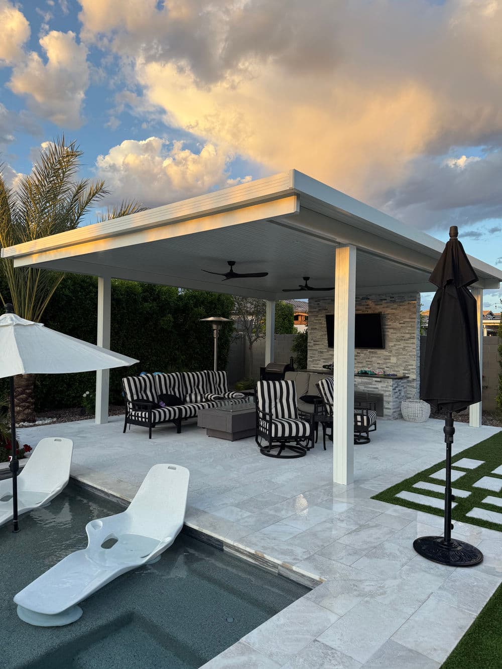 Modern outdoor patio with seating, poolside loungers, and stylish design under a blue sky.