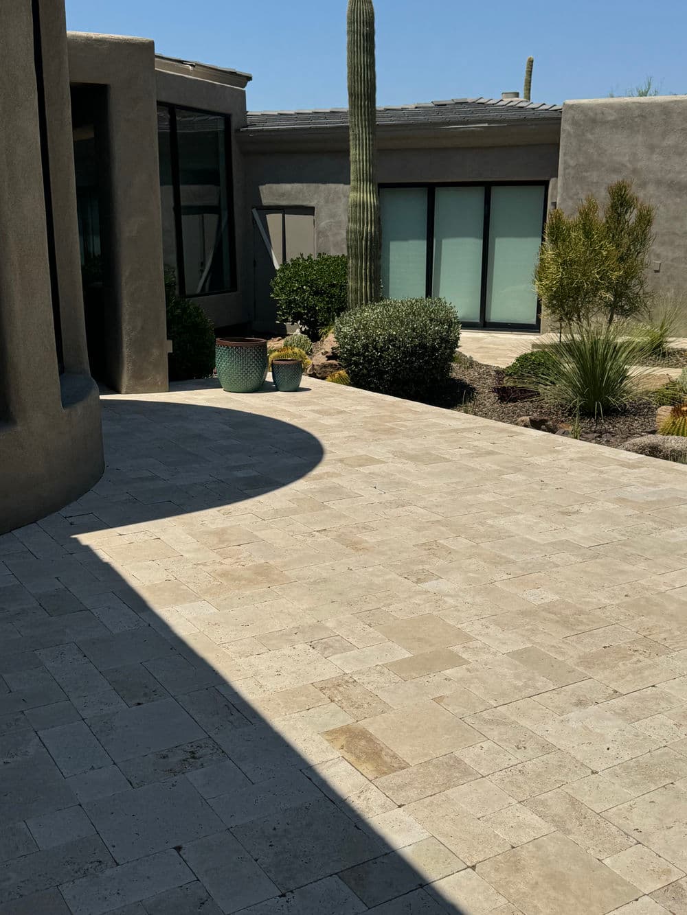 Modern outdoor patio with stone flooring, cacti, and greenery in a sunny setting.
