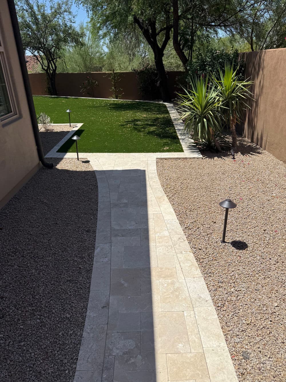 Curved stone pathway leading to a lush green lawn surrounded by desert landscaping.