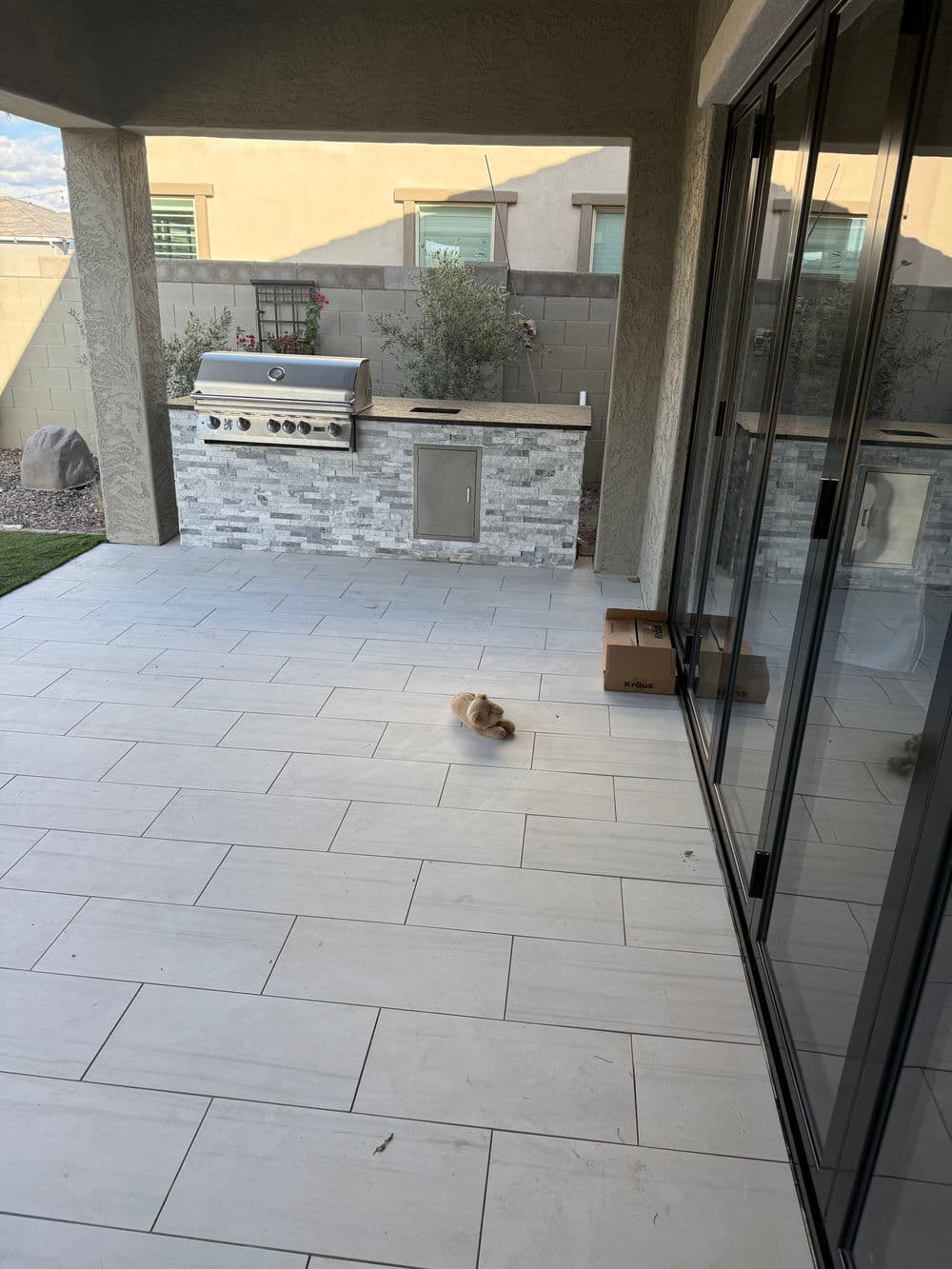 Cozy outdoor patio with grill, stone features, and a small dog on tiled floor.