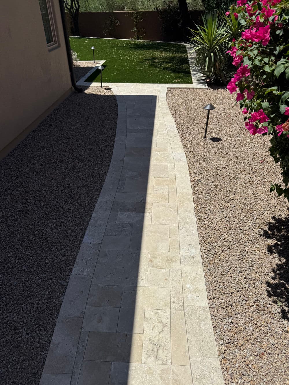 Curved stone pathway leading to lush lawn, bordered by vibrant bougainvillea flowers.