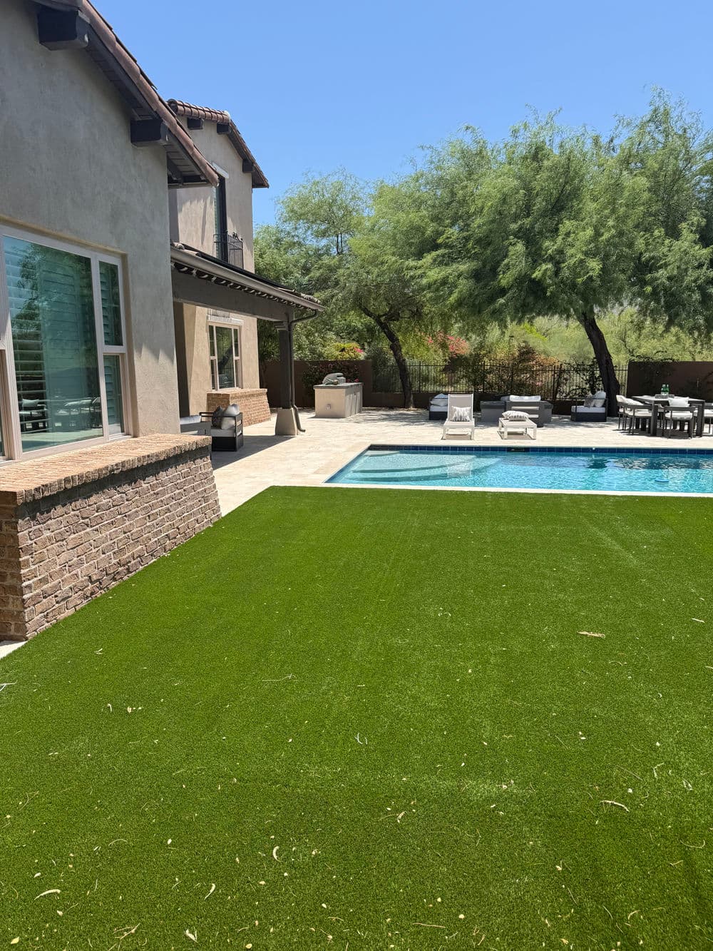 Modern backyard with artificial grass, pool, and lounge area in sunny outdoor setting.