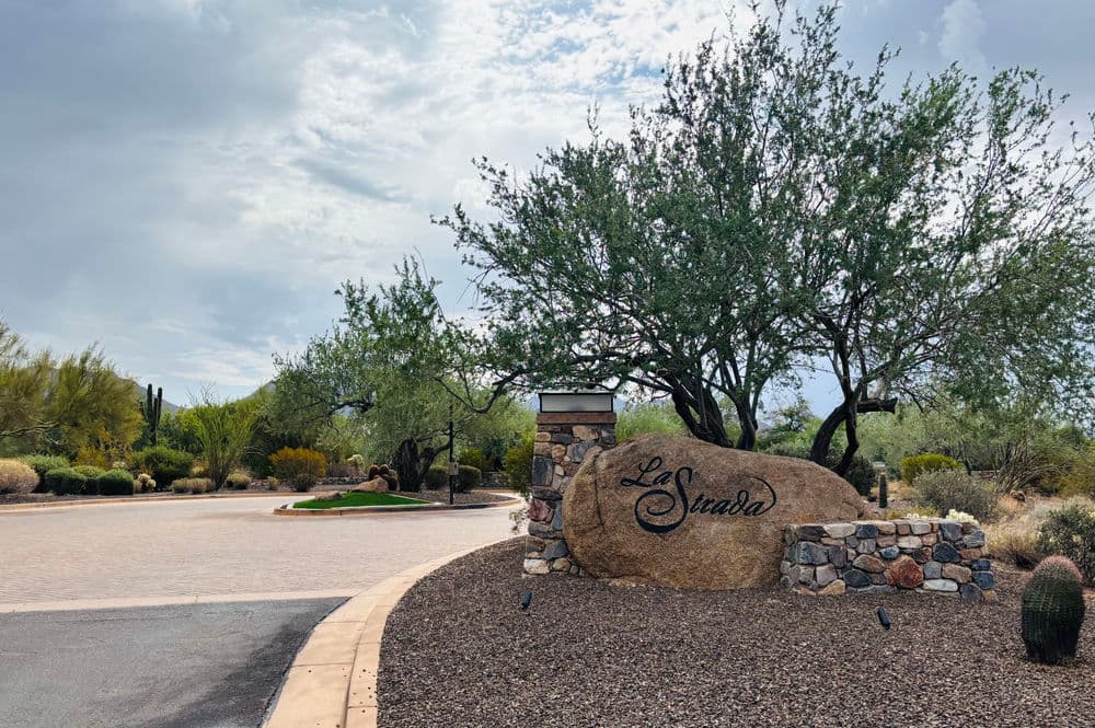 La Suada entrance sign with desert landscaping and cloudy sky in Arizona.