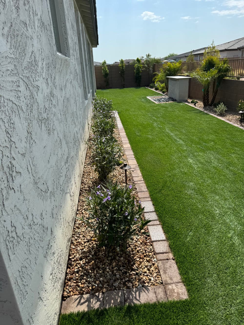 Lush green lawn with flower beds along a home's side, bright sunny day.