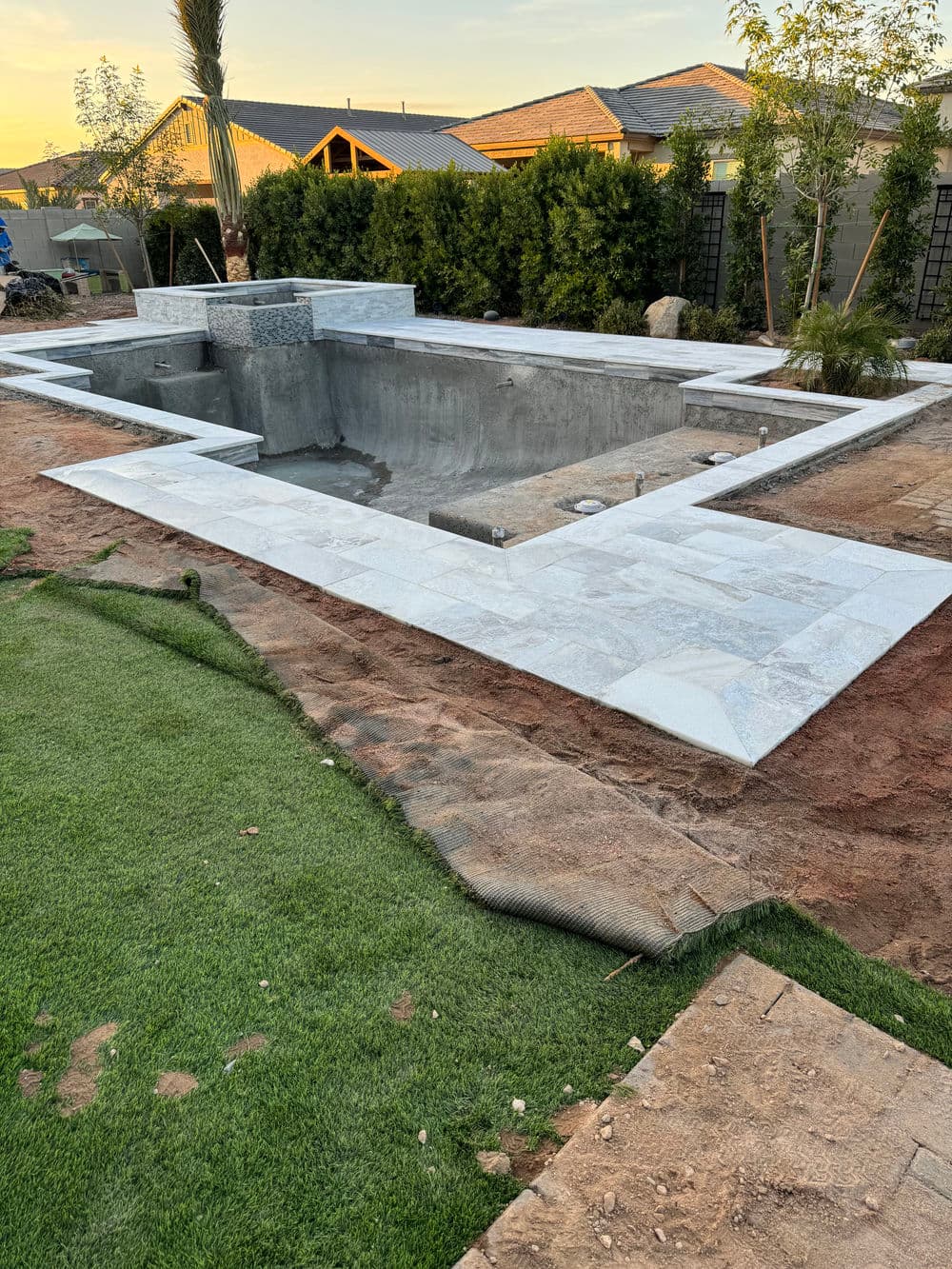 In-ground swimming pool under construction with stone tiles and landscaped surroundings.