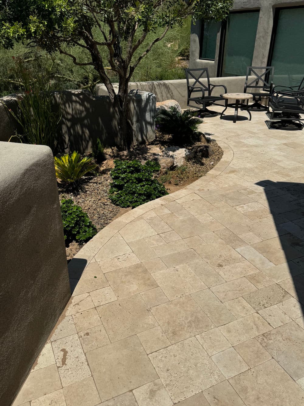 Modern patio featuring stone tile, greenery, and seating area surrounded by low plants.