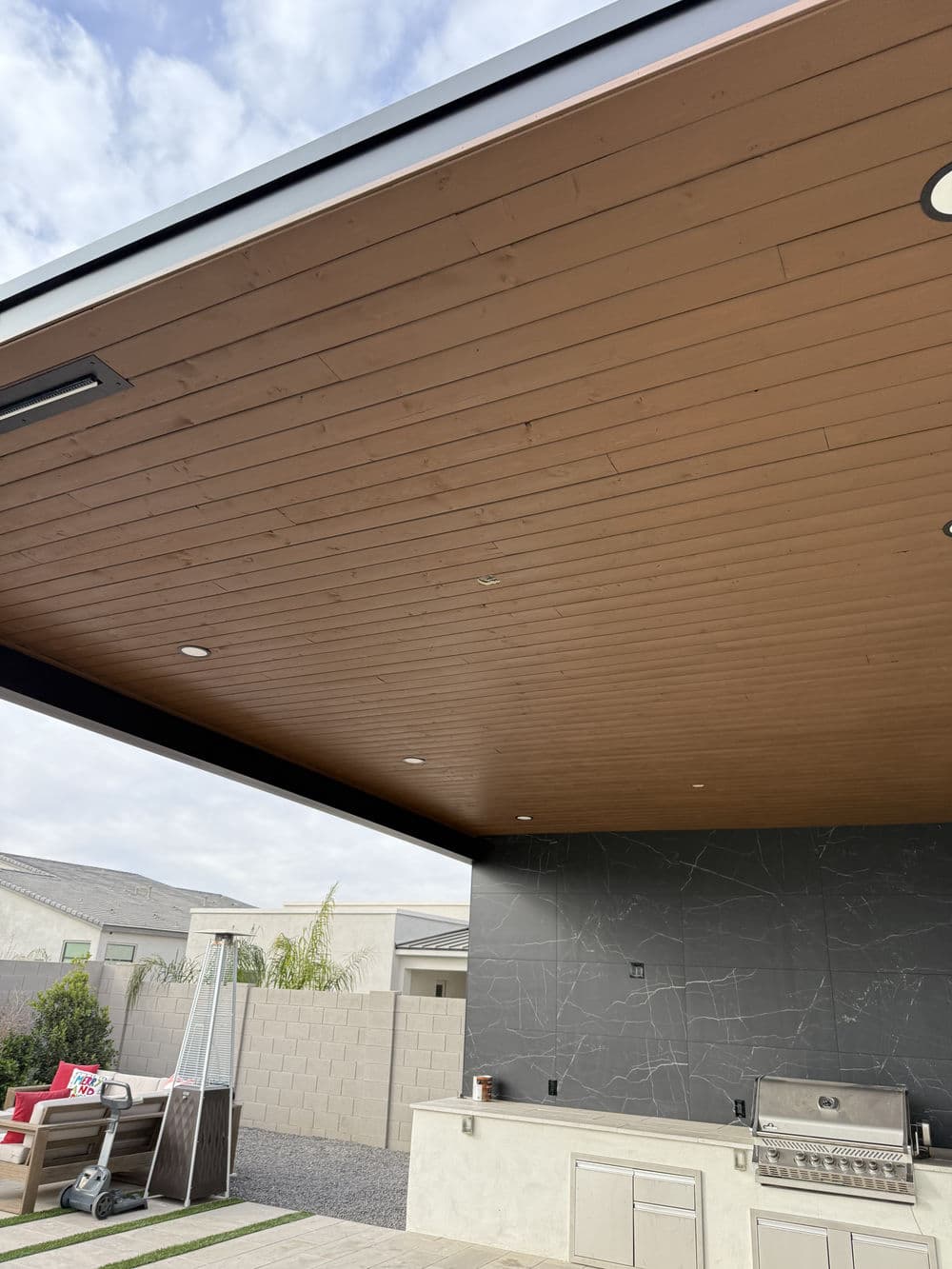 Modern outdoor kitchen with wooden ceiling and integrated lighting, featuring a sleek grill.