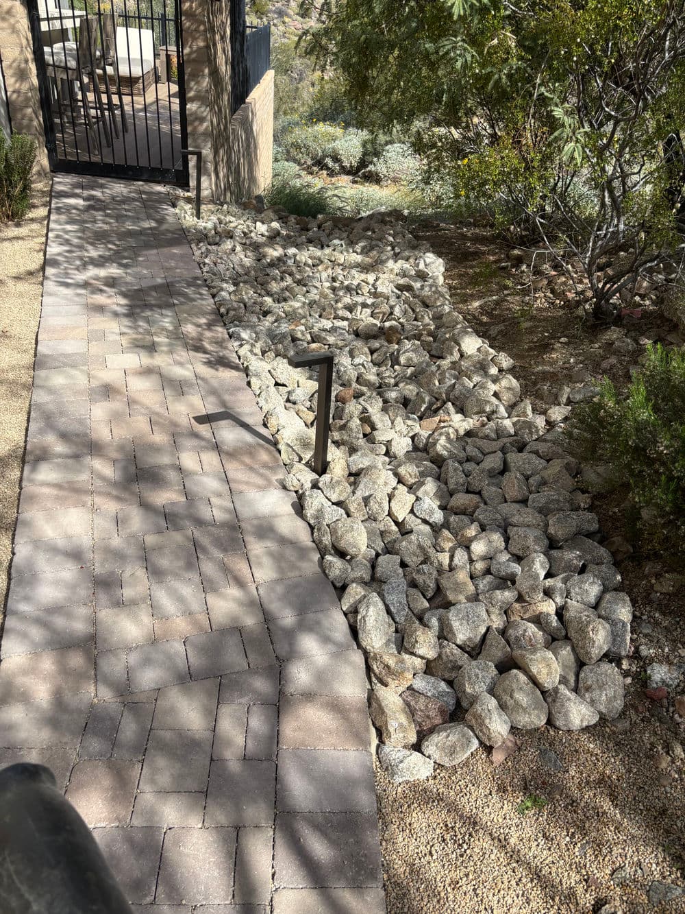 Landscape pathway with paver stones and decorative rocky drainage bed in a garden setting.