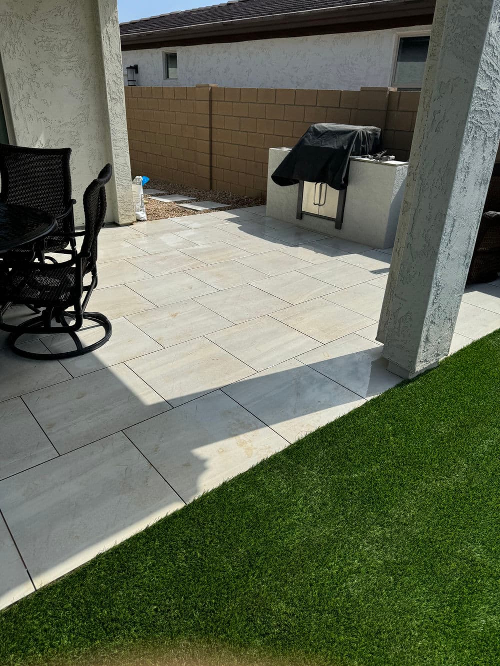 Patio with tiled floor, outdoor grill, and artificial grass in a residential backyard setting.