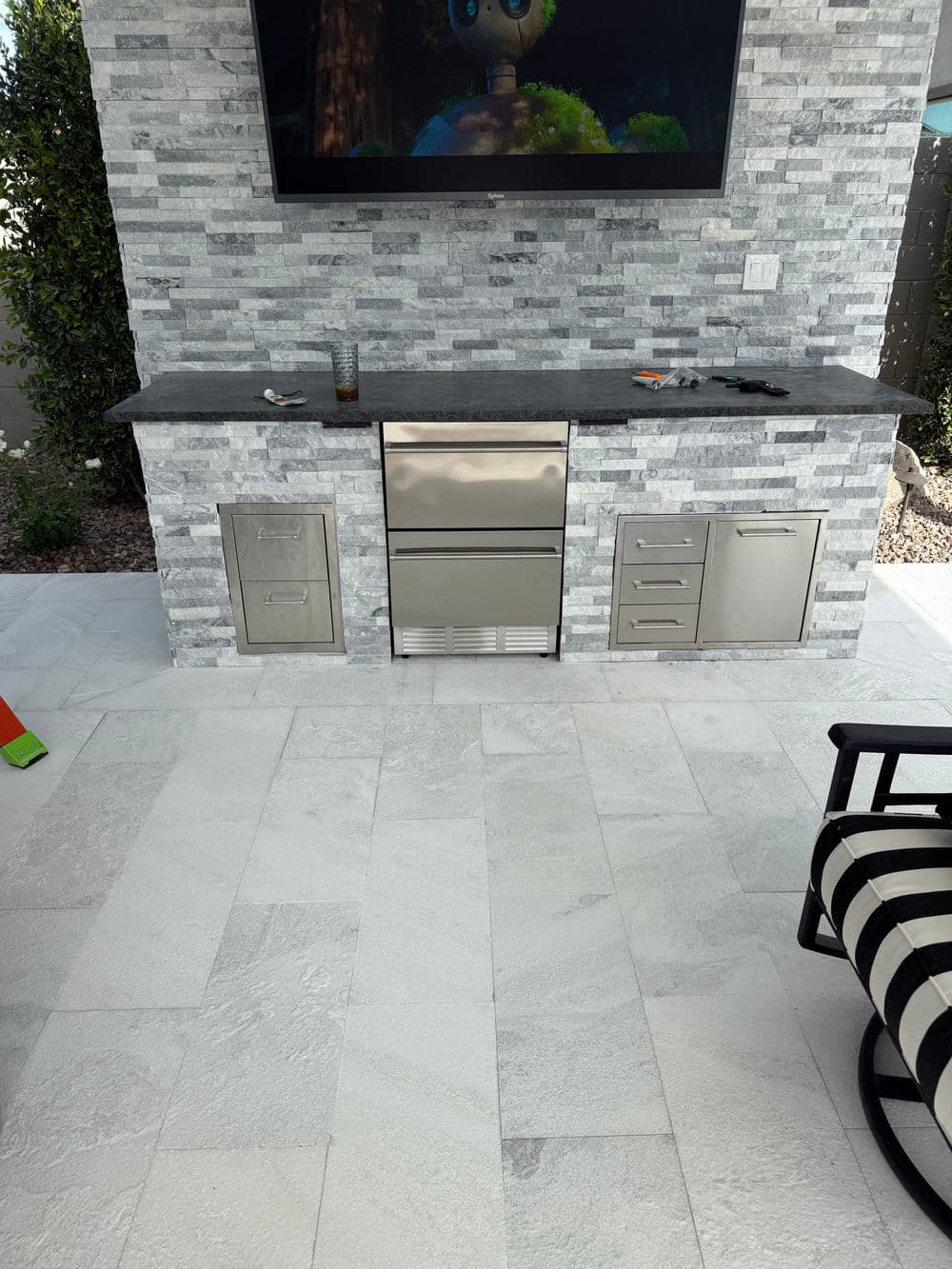 Outdoor kitchen setup featuring stainless steel appliances, stone walls, and modern flooring.