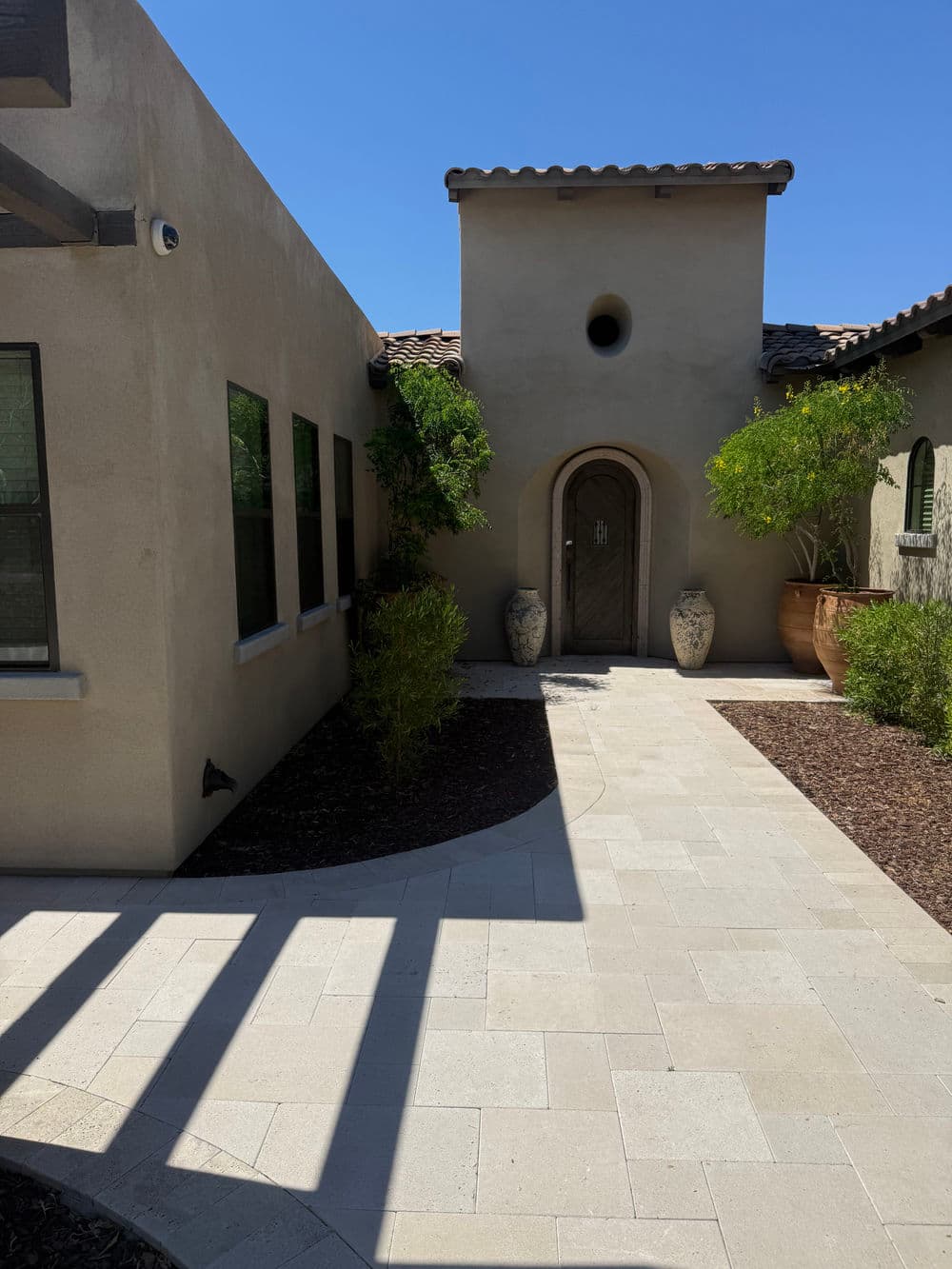 Desert-style home entrance with stone pathway, planters, and potted plants under blue sky.