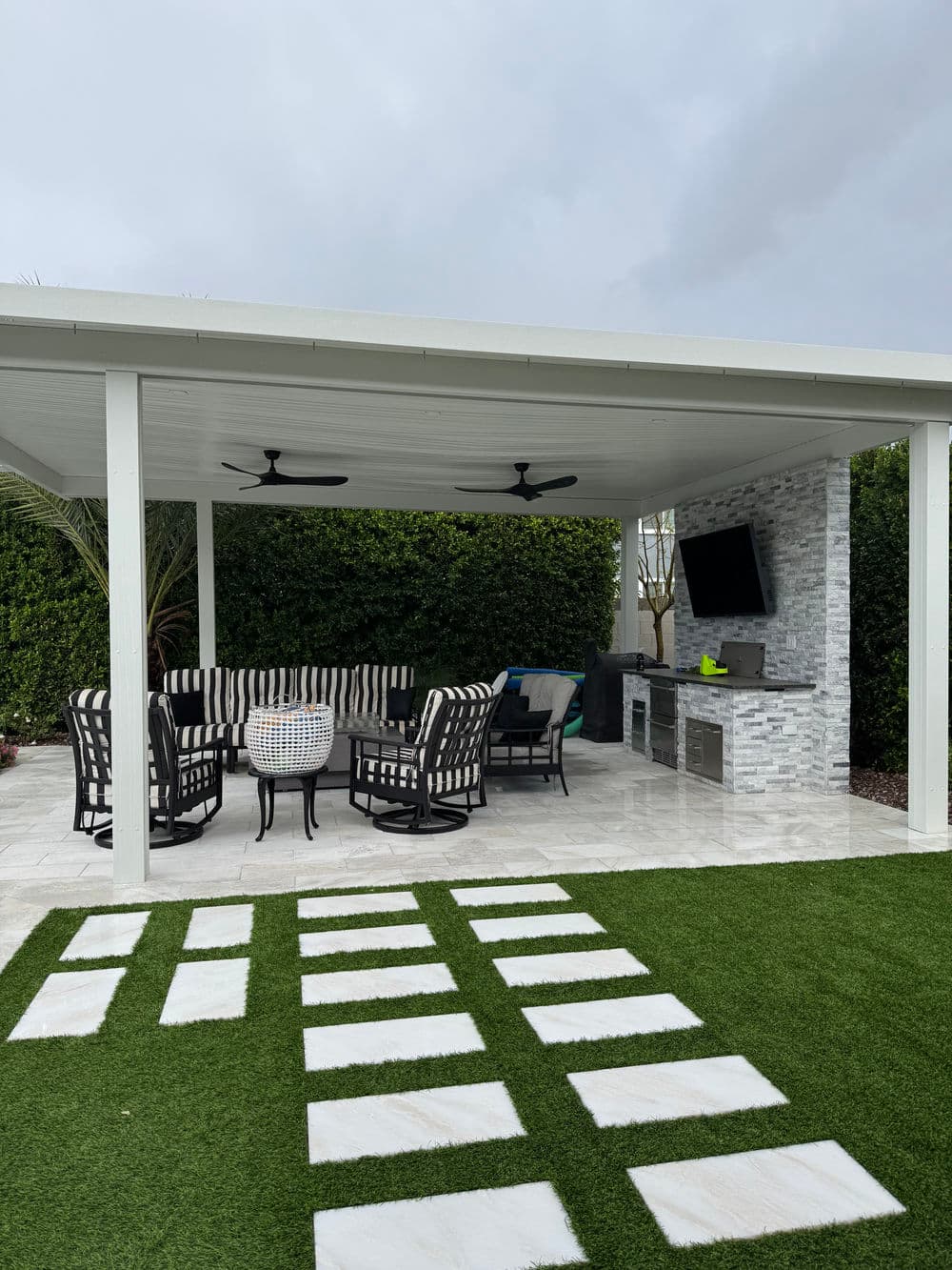 Modern outdoor patio with seating, outdoor kitchen, stone accents, and artificial turf.