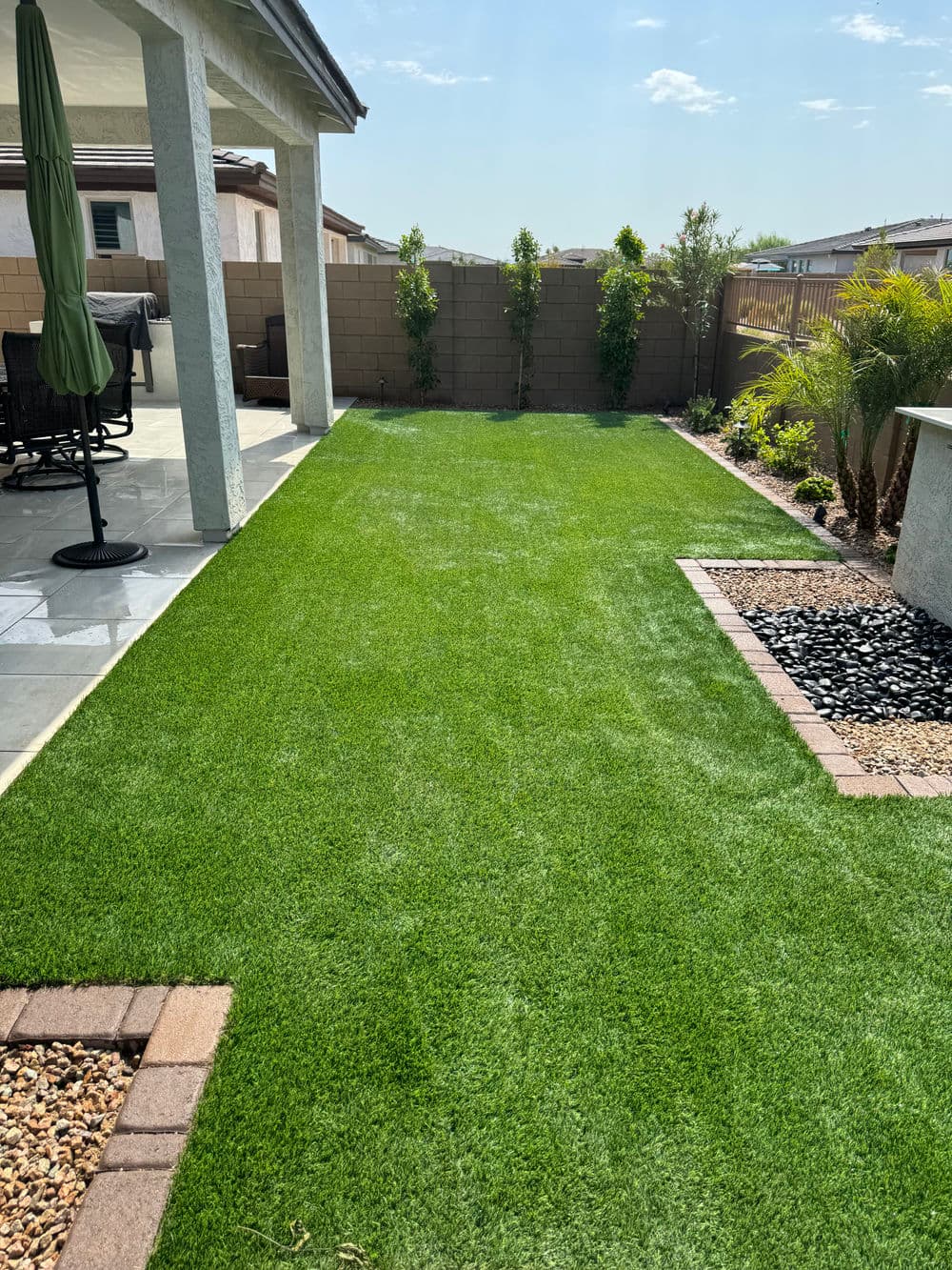 Lush green artificial lawn in a modern backyard with decorative stones and plants.