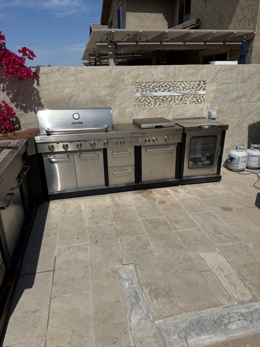 Outdoor kitchen with stainless steel grill, countertop, and flower garden background.