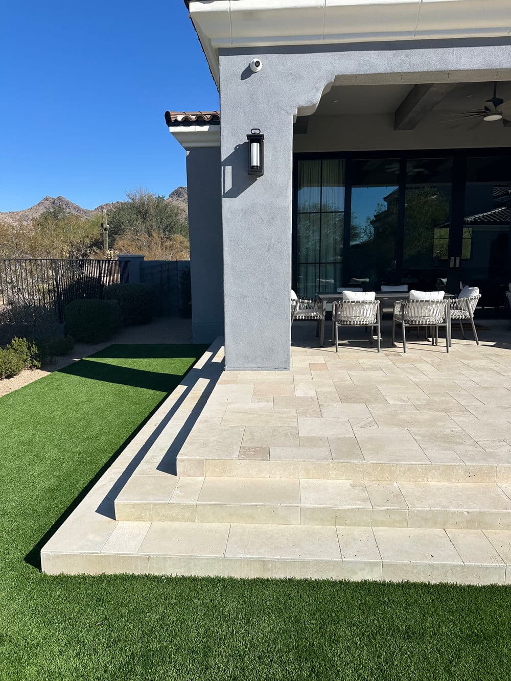Modern home patio with stone pavers, green artificial grass, and mountain view in background.