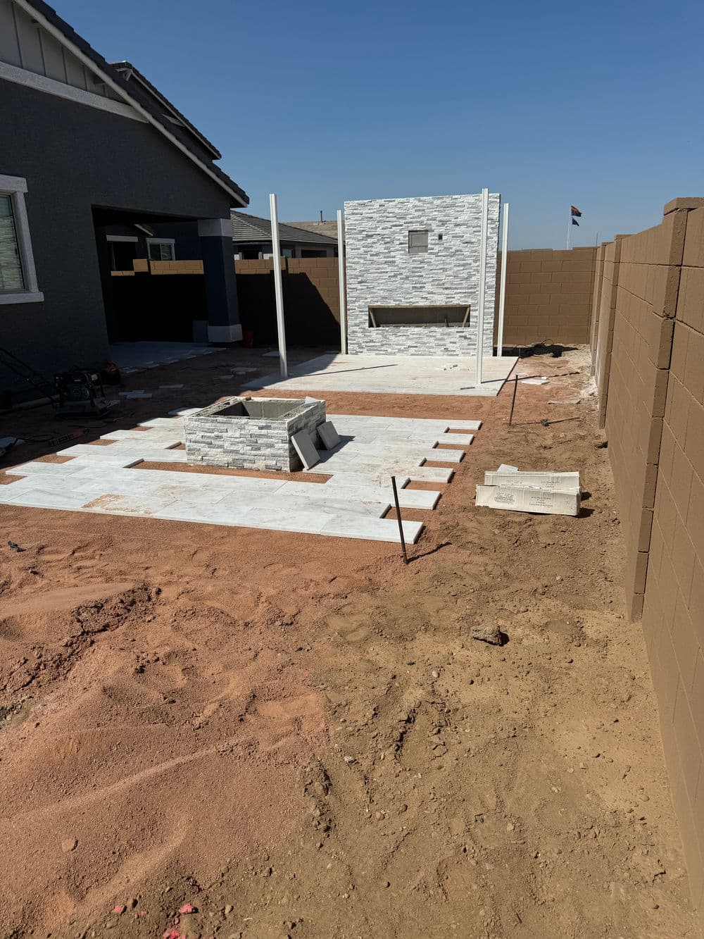 Backyard with stone fireplace and unfinished patio area, surrounded by brown fencing.