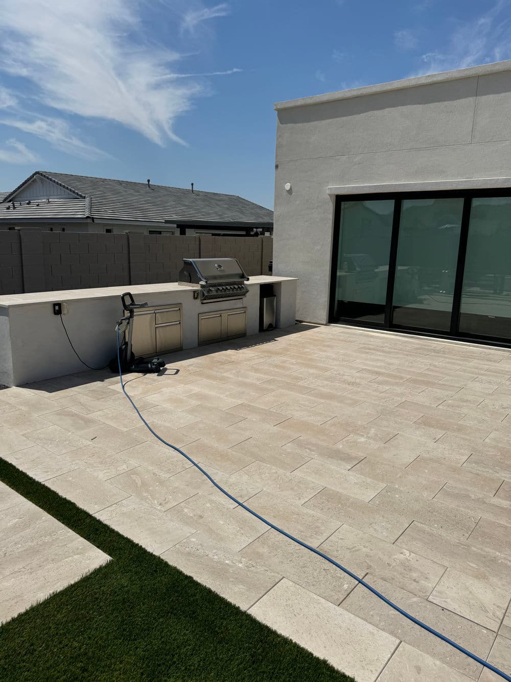 Outdoor patio with a built-in grill and modern stone tiles under a clear blue sky.