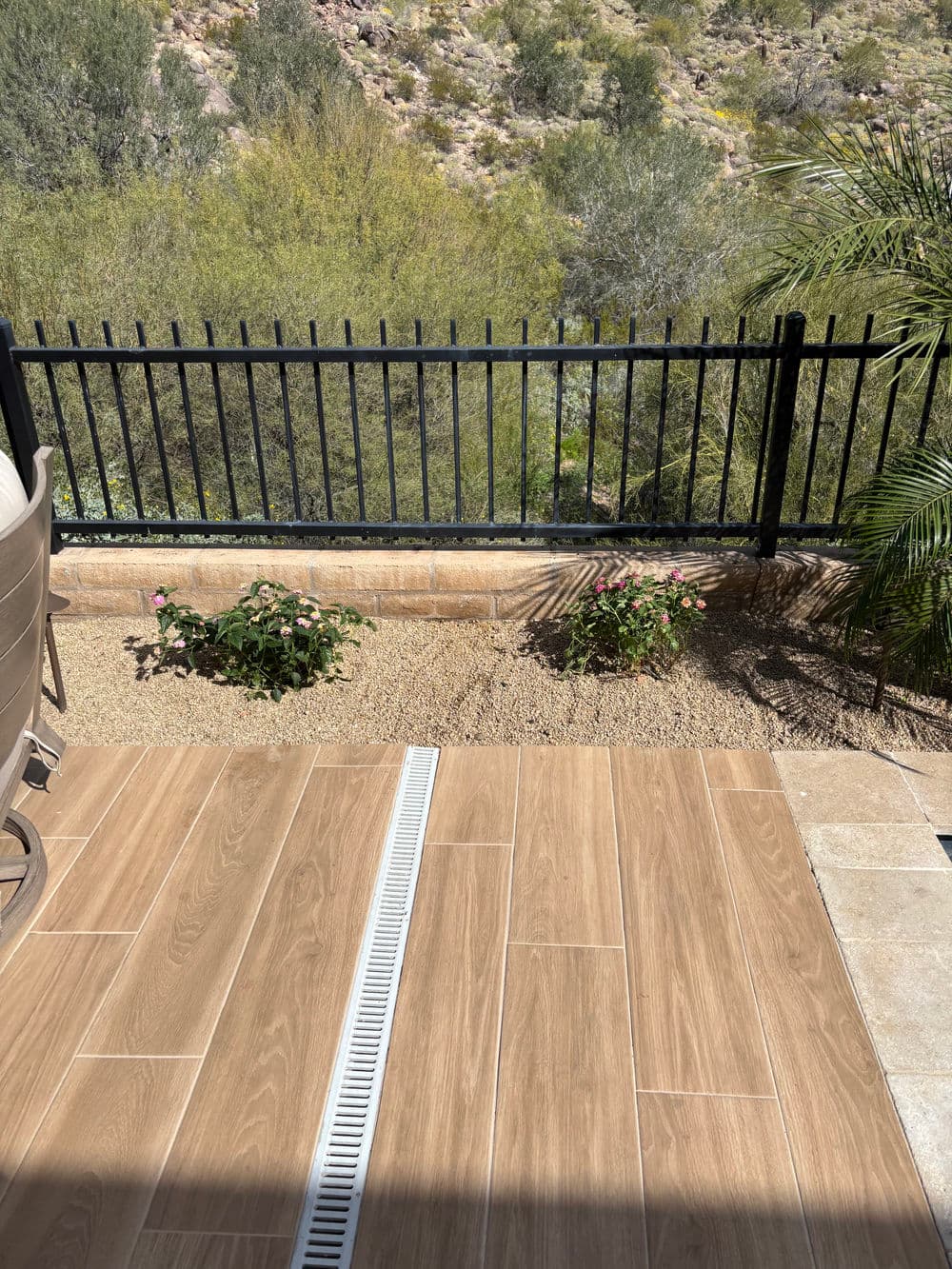 Desert patio with wooden tiles, black fence, and lush greenery in the background.
