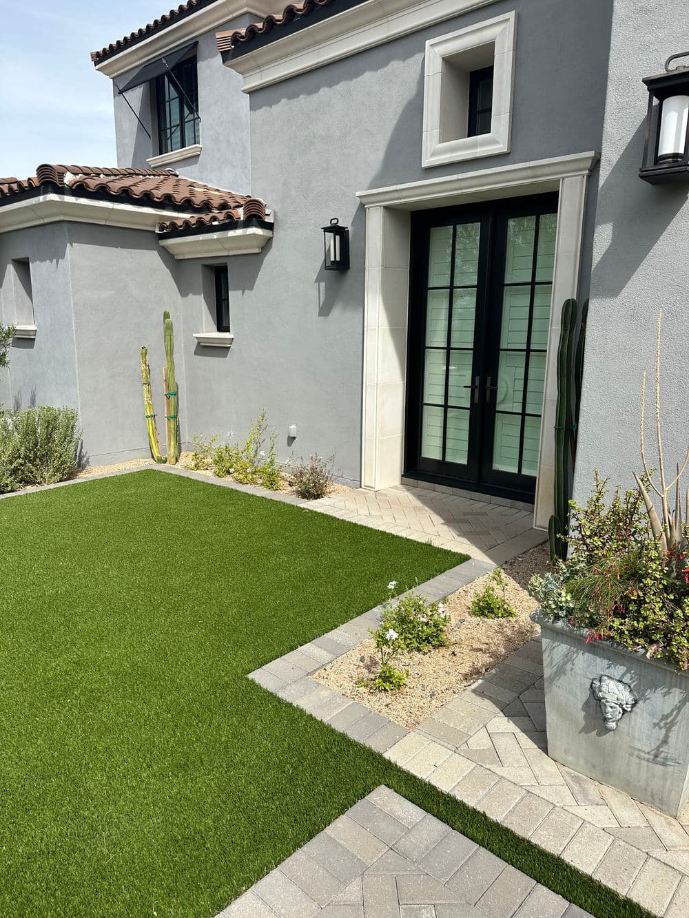 Modern home exterior with lush artificial grass, pavers, and desert landscaping details.