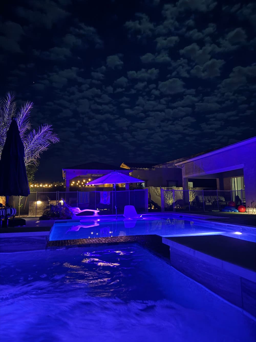Modern backyard pool with luminous blue lighting and cloud-covered night sky.