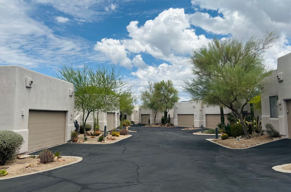 Desert community with modern homes, palm trees, and cloudy blue sky.