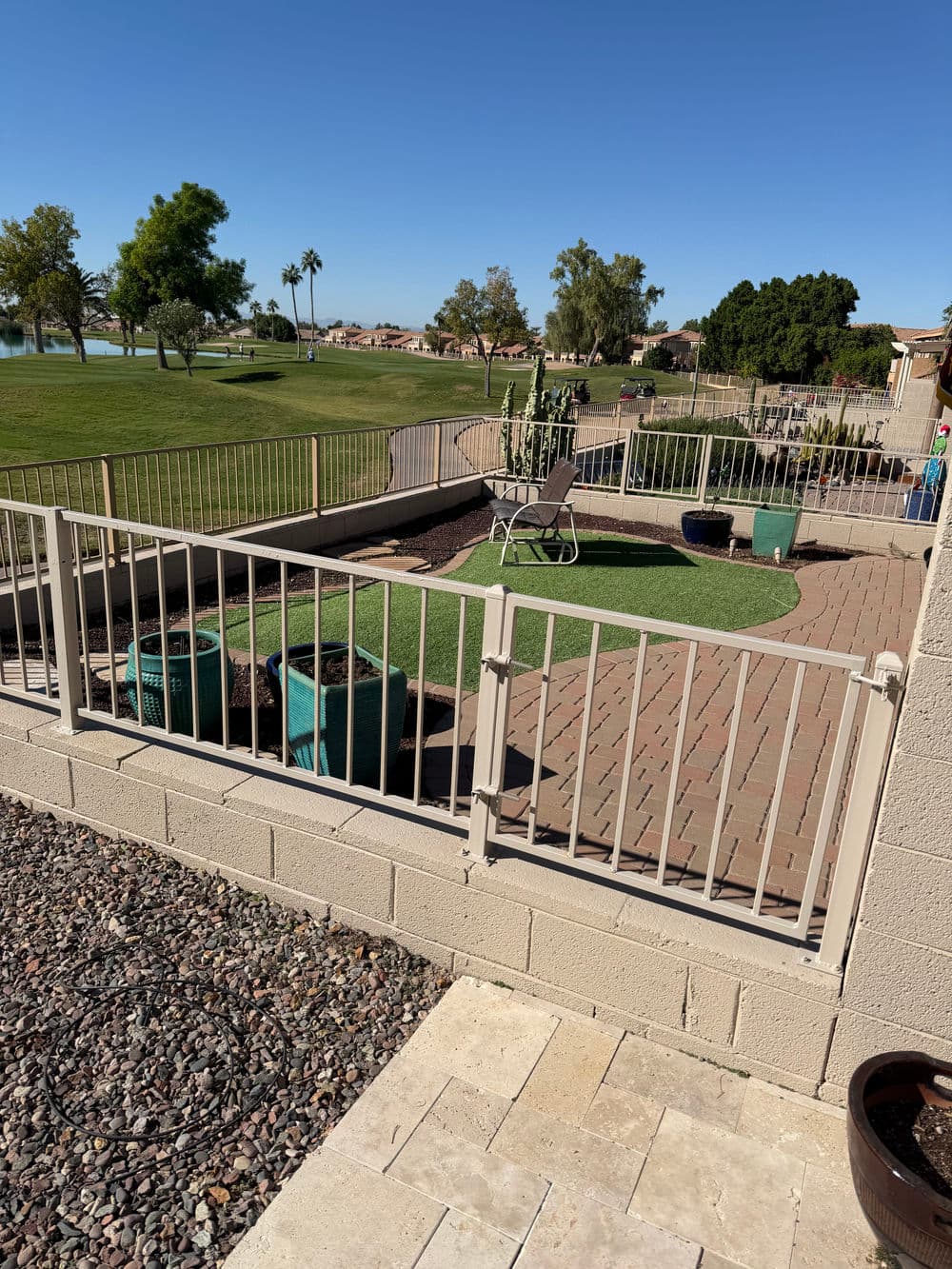 Landscaped yard with decorative fencing, green lawn, and planters overlooking a golf course.