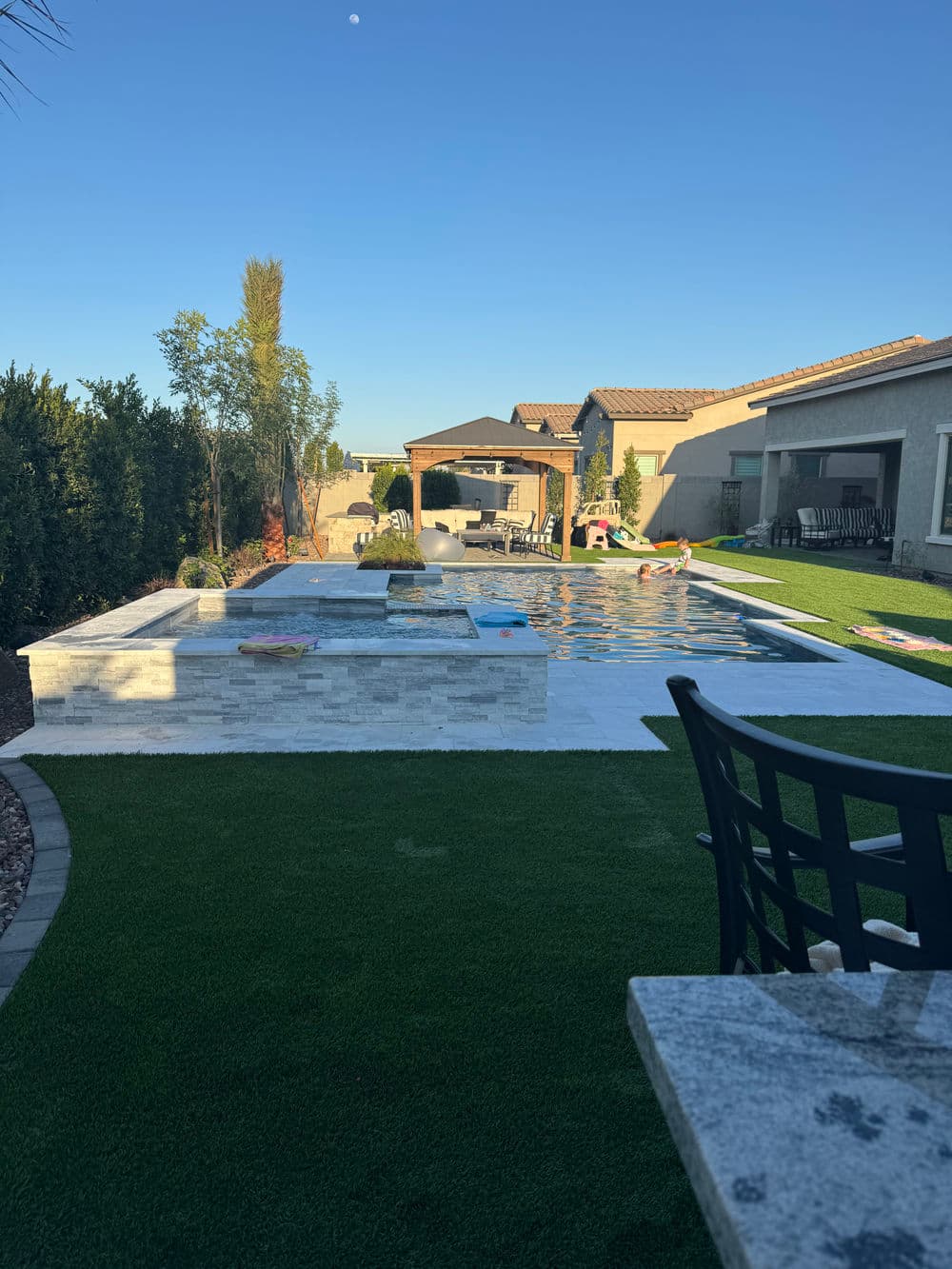 Stylish backyard with a pool, lounge area, and landscape design under clear blue sky.