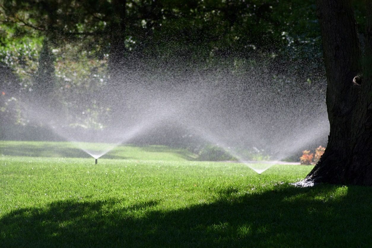 A lawn with sprinklers spraying water on it.