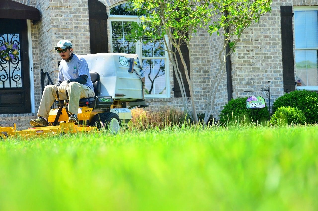 A man riding on the back of a yellow lawn mower.